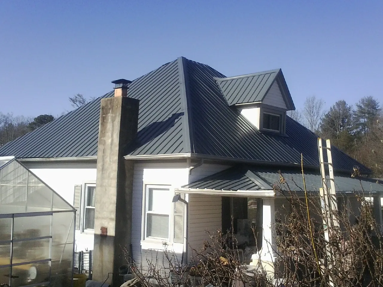 Dark blue standing seam metal roof on a white farmhouse with dormer — Slate & Tile Roof Repair by Roofing Brothers in Tabor City