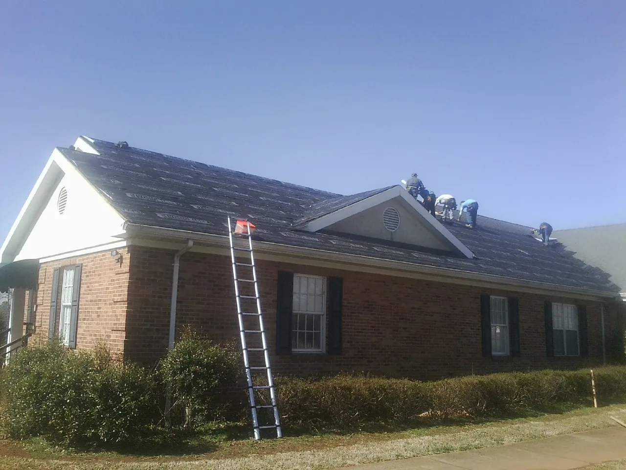Crew tearing shingles off a brick ranch roof with a ladder set — Emergency Roof Repair work by our crew in Tabor City
