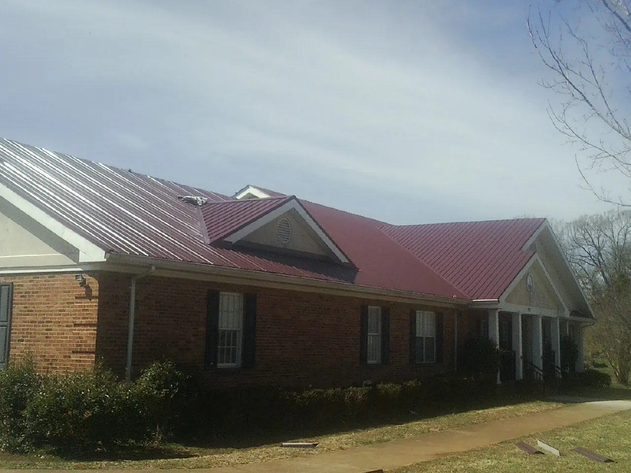 Red metal roof with gabled entries on a long brick building, from a Hail Damage Roof Repair job in Tabor City