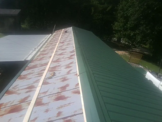 Old rusted panels beside newly installed green metal roofing — Wind Damage Roof Repair by Roofing Brothers in Tabor City