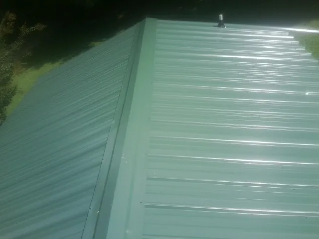 New green metal panels meeting at the ridge of a roof — Flat Roof Repair work by our crew in Tabor City