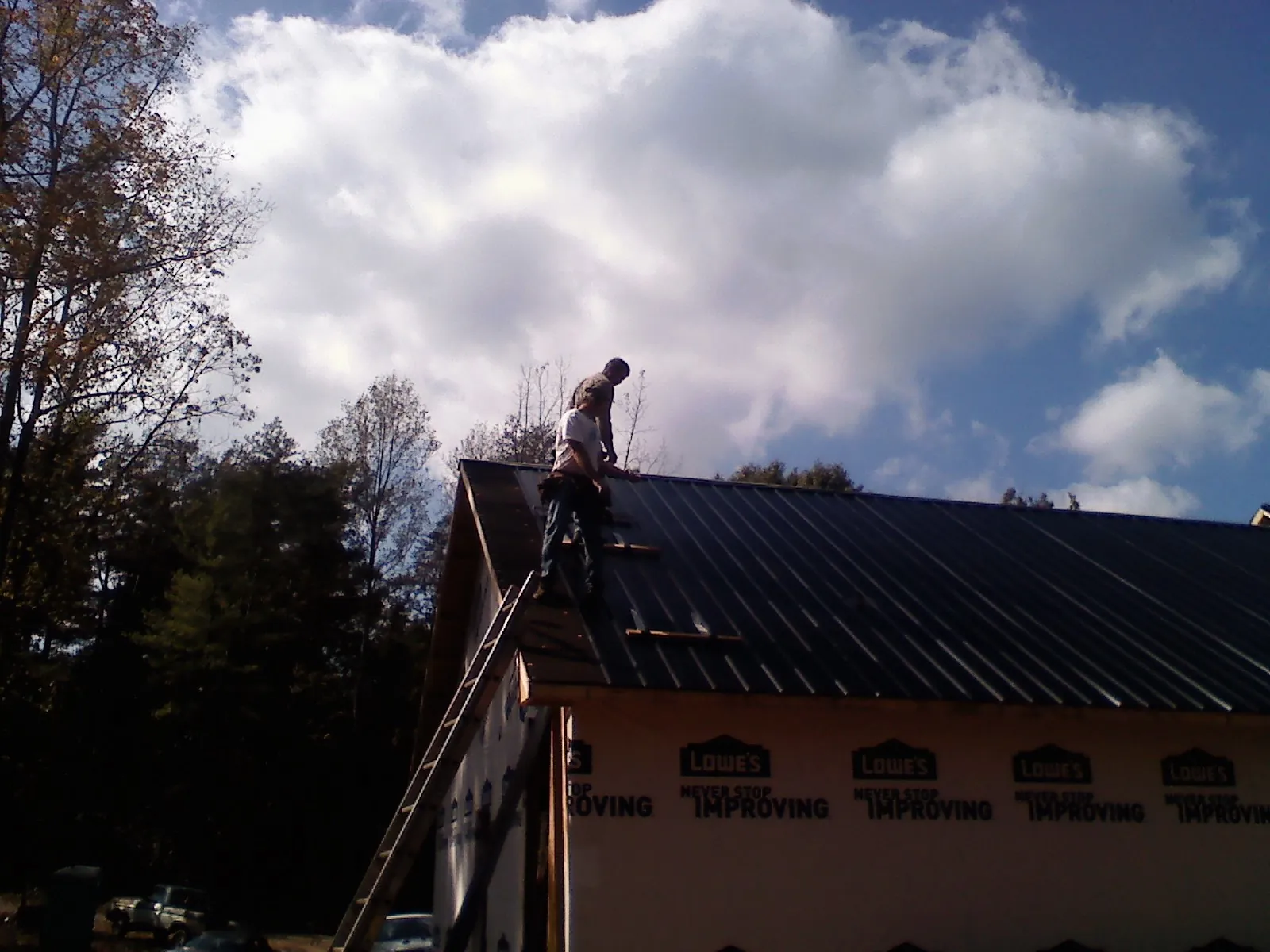 Roofer fastening dark metal panels high against a cloudy sky, from a Roof Inspection job in Tabor City