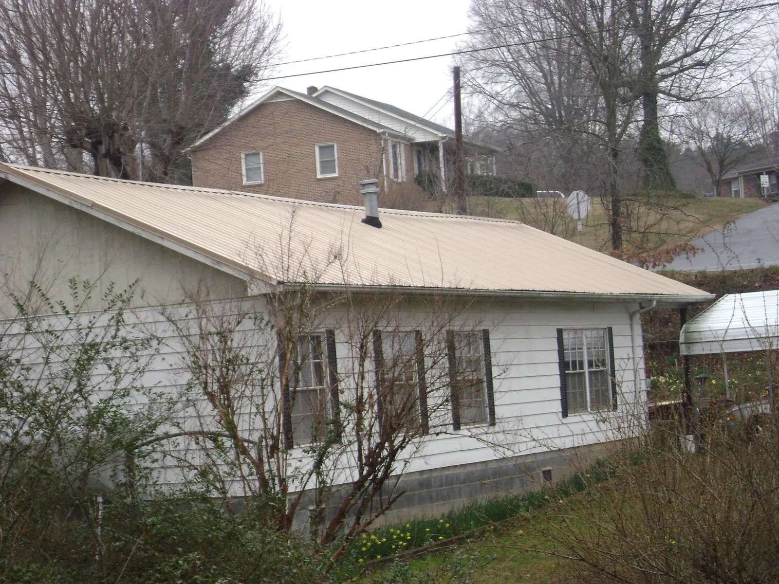 Tan metal roof on a white sided house set into a hillside — Commercial Roofing by Roofing Brothers in Tabor City