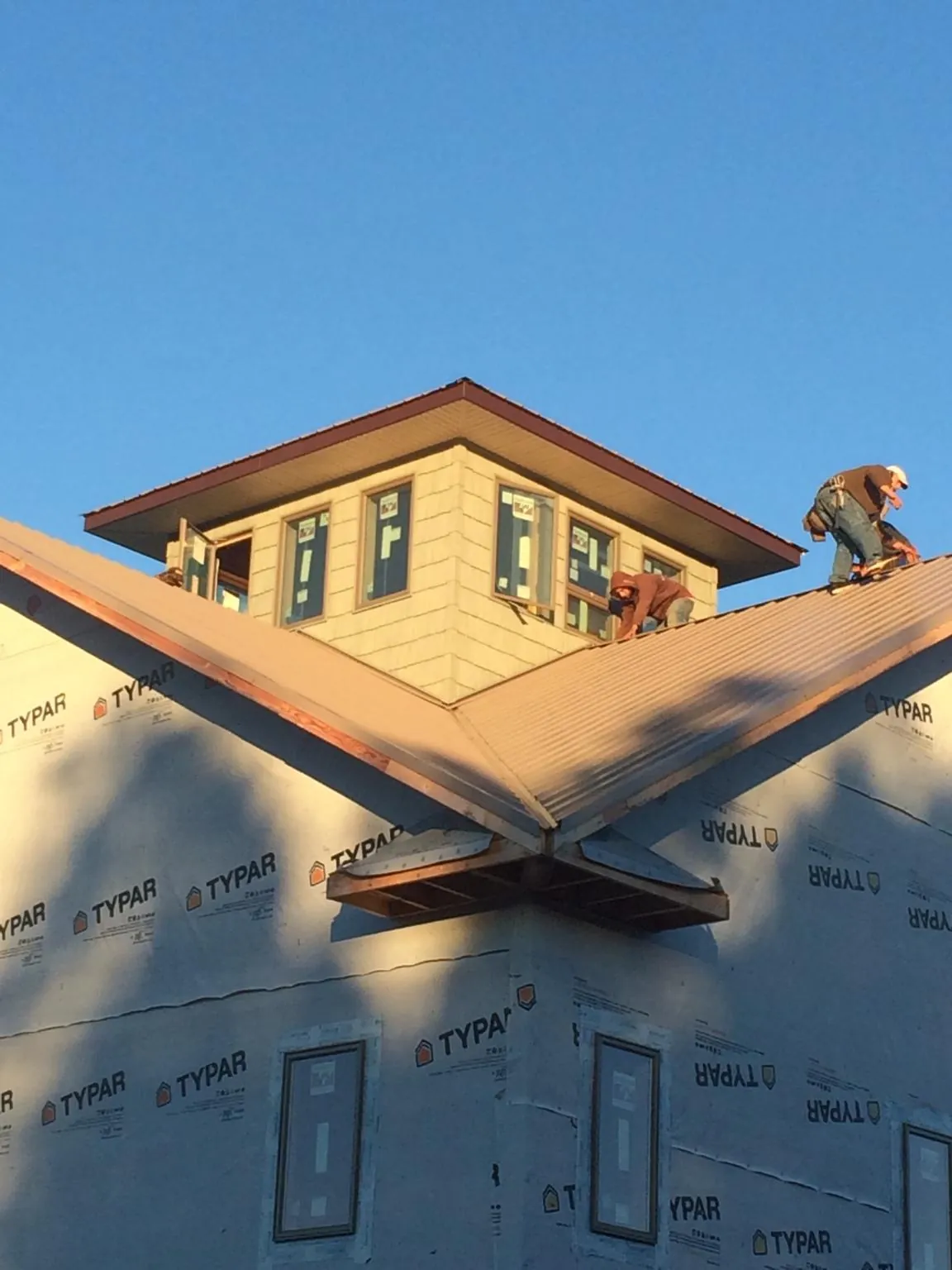 Roofers working around a rooftop cupola on a new metal roof at sunset — Roof Waterproofing in Tabor City by Roofing Brothers